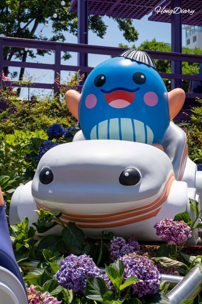Festival mascot character posing beside hydrangea displays at Jangsaengpo