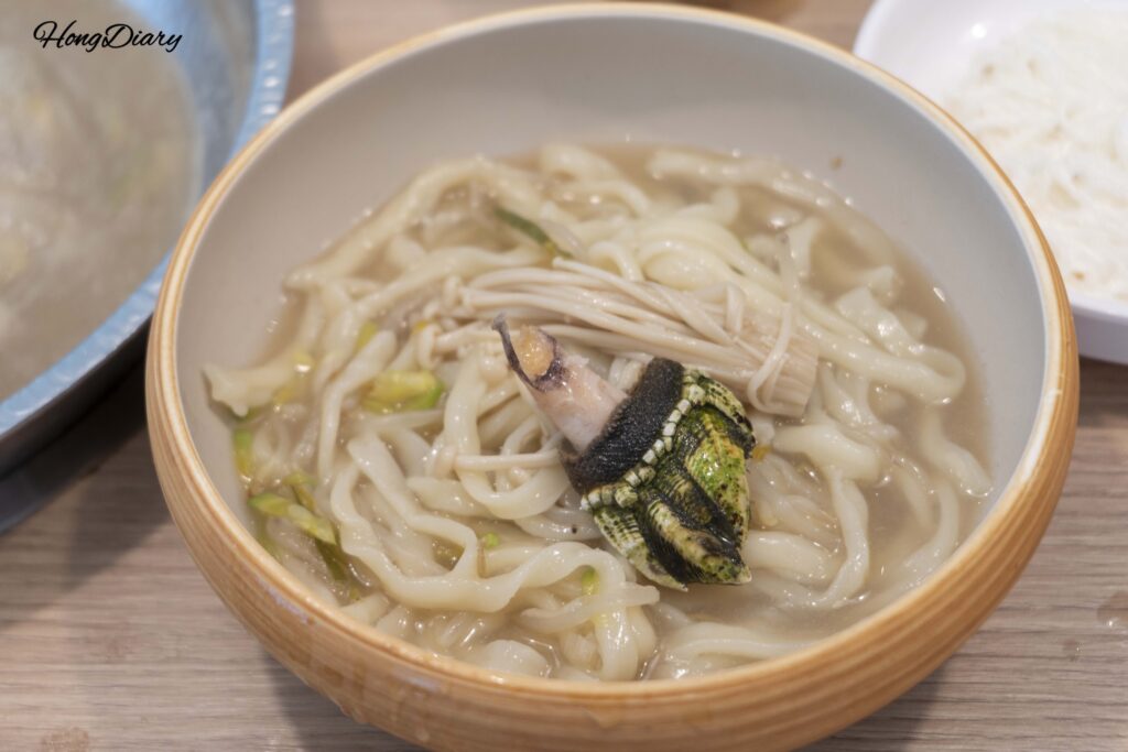 Final bowl of kalguksu noodles topped with goose barnacles in layered shabu broth at Cosmos Busan