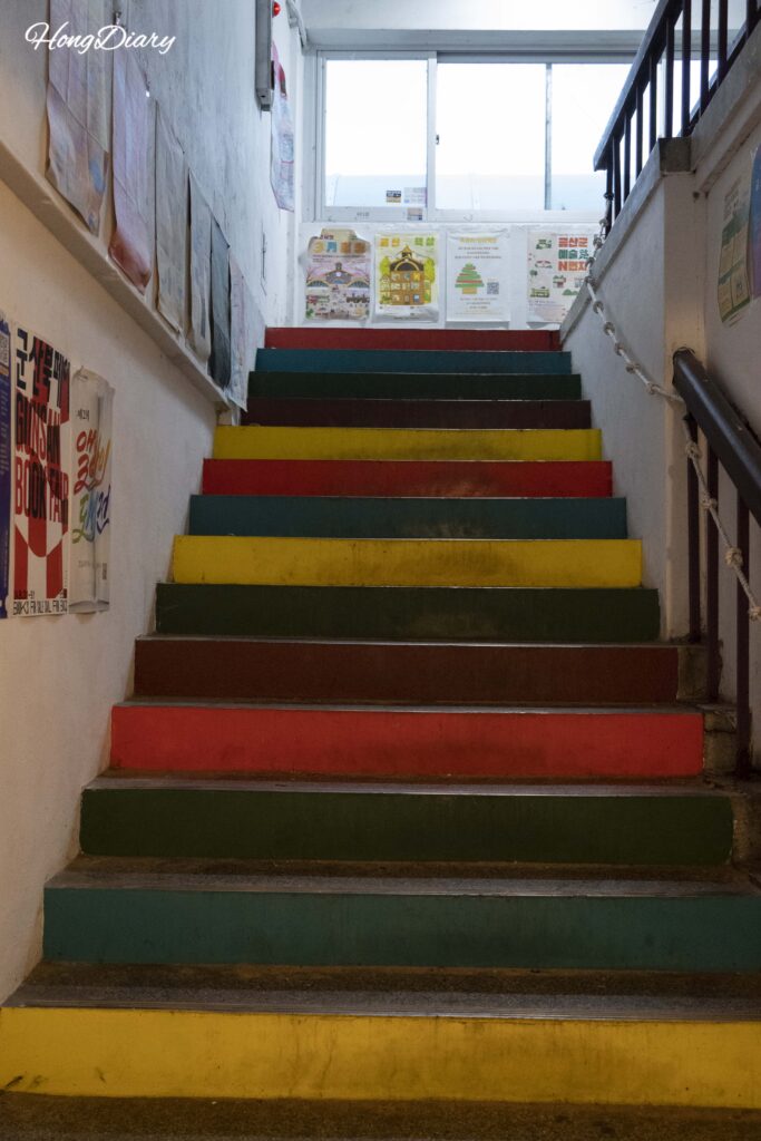 Escalera colorida que sube al segundo piso donde está Durumi Bookshop en el Mercado Geumbit, Geumsan