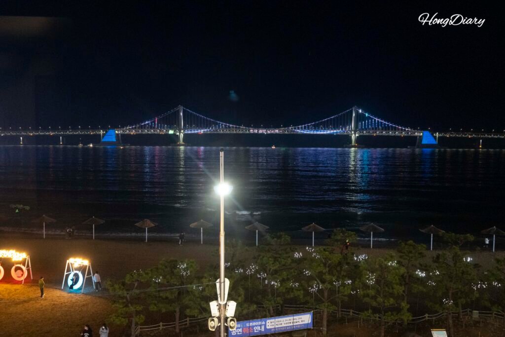 Copa de vino frente a la ventana con vista nocturna del Puente Gwangan iluminado desde el Gwangalli W Hotel en Busán