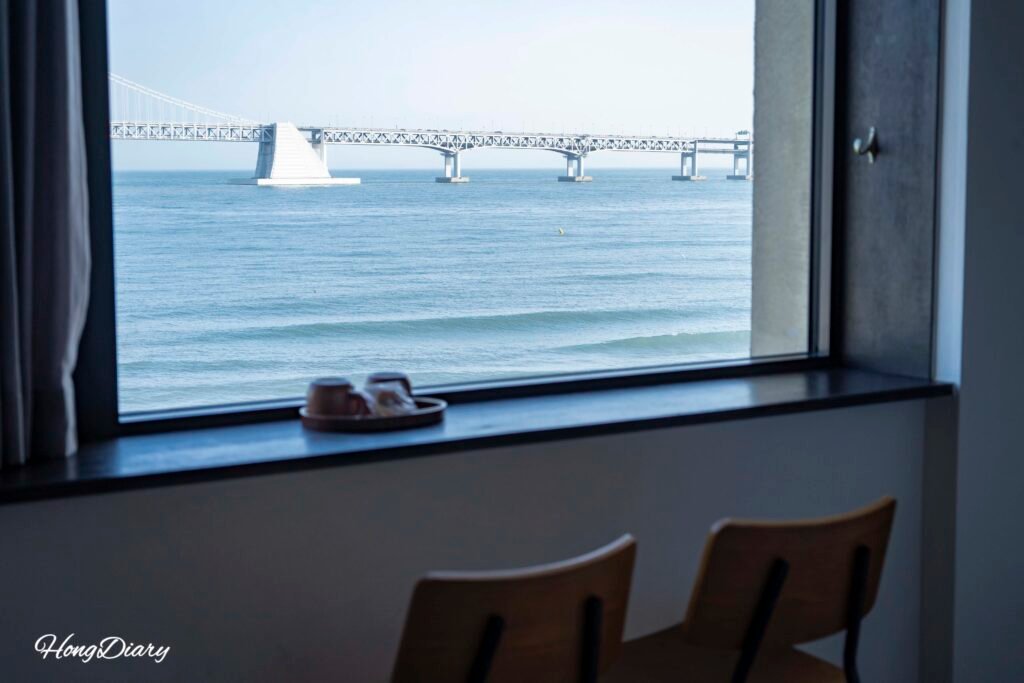 Set de té de frutas deshidratadas y taza de cerámica junto a la ventana del Gwangalli W Hotel, con vista a la playa de Gwangalli y el Puente Gwangan