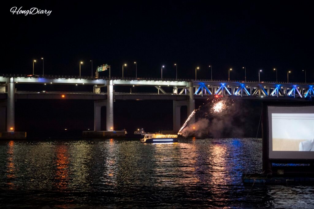 Gwangan Bridge illuminated at night with yacht lights and fireworks over the water in Gwangalli, Busan