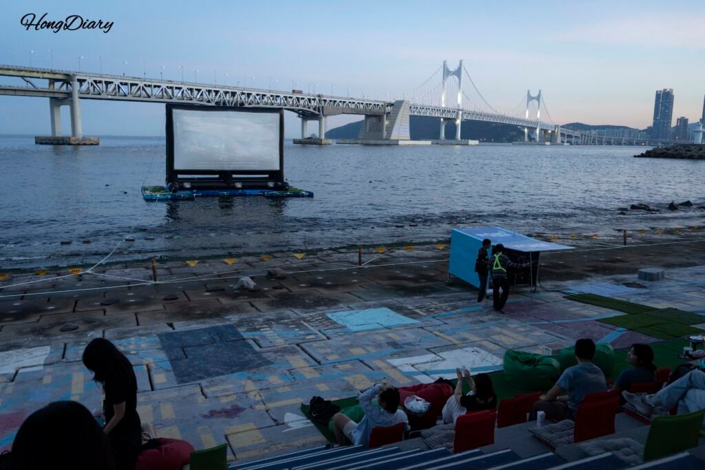 Pantalla de Millak Ocean Cinema al atardecer con el Puente Gwangan visible al fondo en Gwangalli