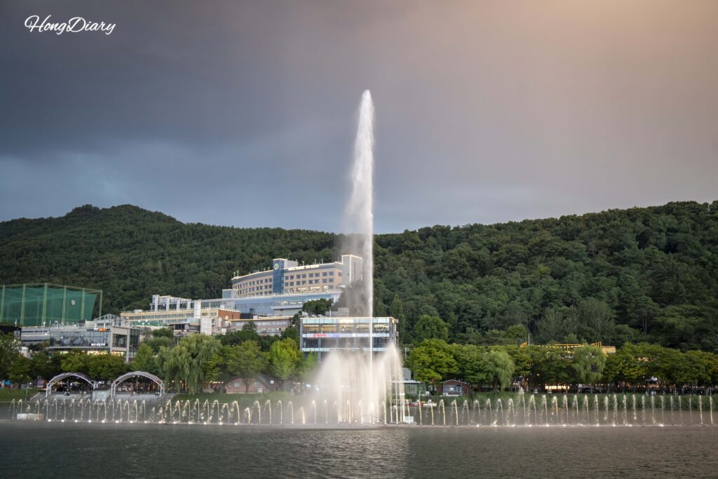 Daytime music fountain show at Suseongmot with water jets shooting from the center of the lake