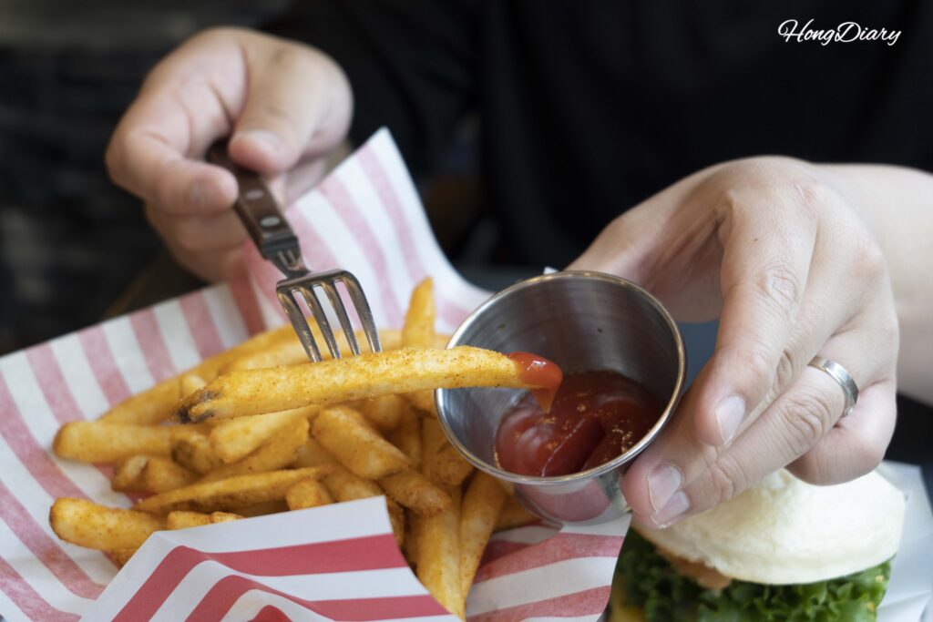 Papas fritas sazonadas de Bao Burger Songjeong siendo sumergidas en kétchup de tomate