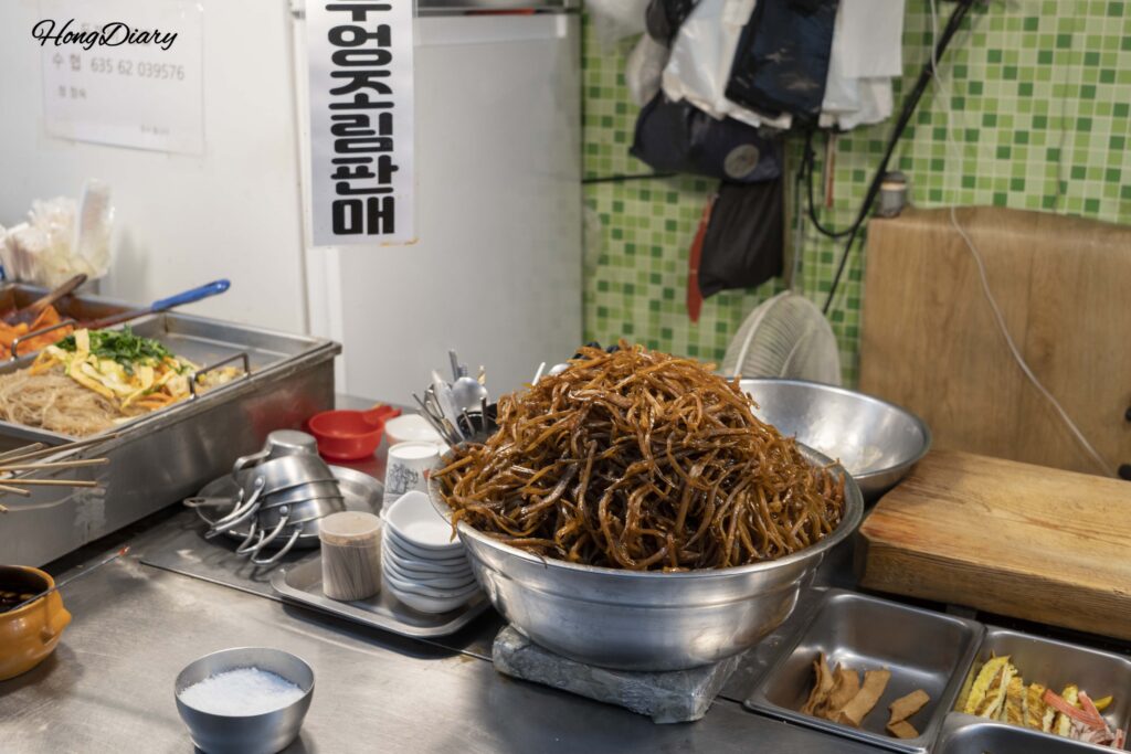 慶州城東市場のごぼうキンパ店先に山積みされたごぼうの煮物と巻きたてのキンパ