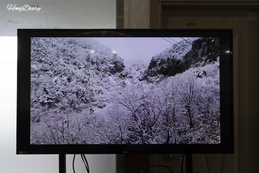 Pantalla en la sala de espera del teleférico mostrando el Geumosan cubierto de nieve en invierno