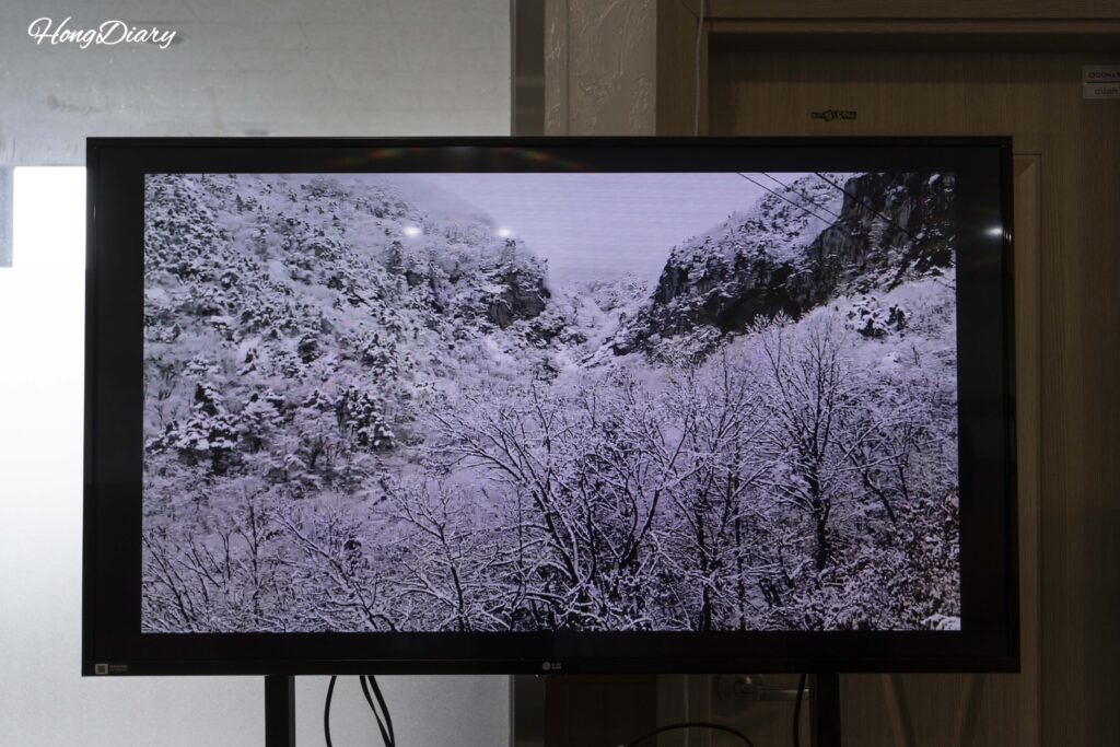 TV screen in the Geumosan cable car waiting room showing winter mountain scenery