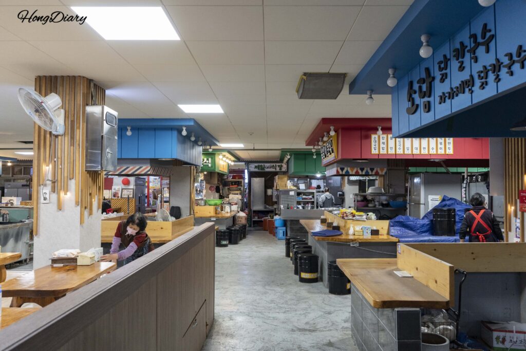Narrow walkway inside the food alley of Jinju Jungang Market with restaurant signs and stalls