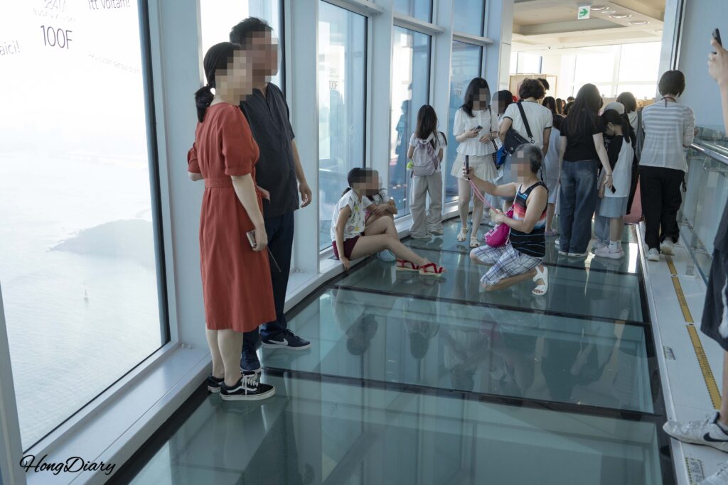 Tourists taking photos at the panoramic window on the 100th floor of Busan X the Sky