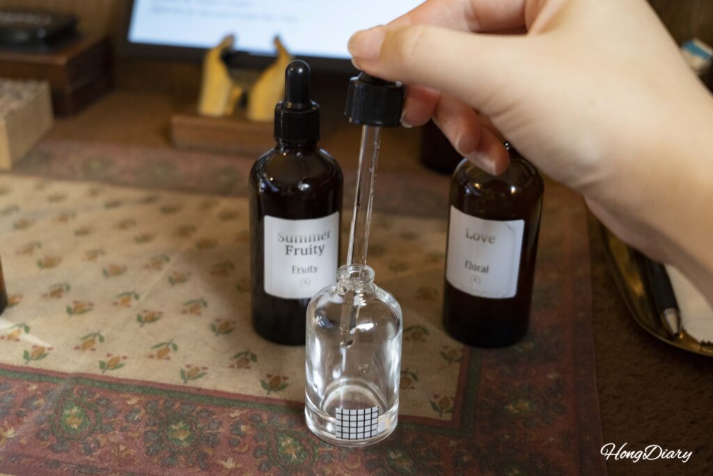 Hands blending custom perfume oils into an empty bottle at ADoR Gwangalli workshop
