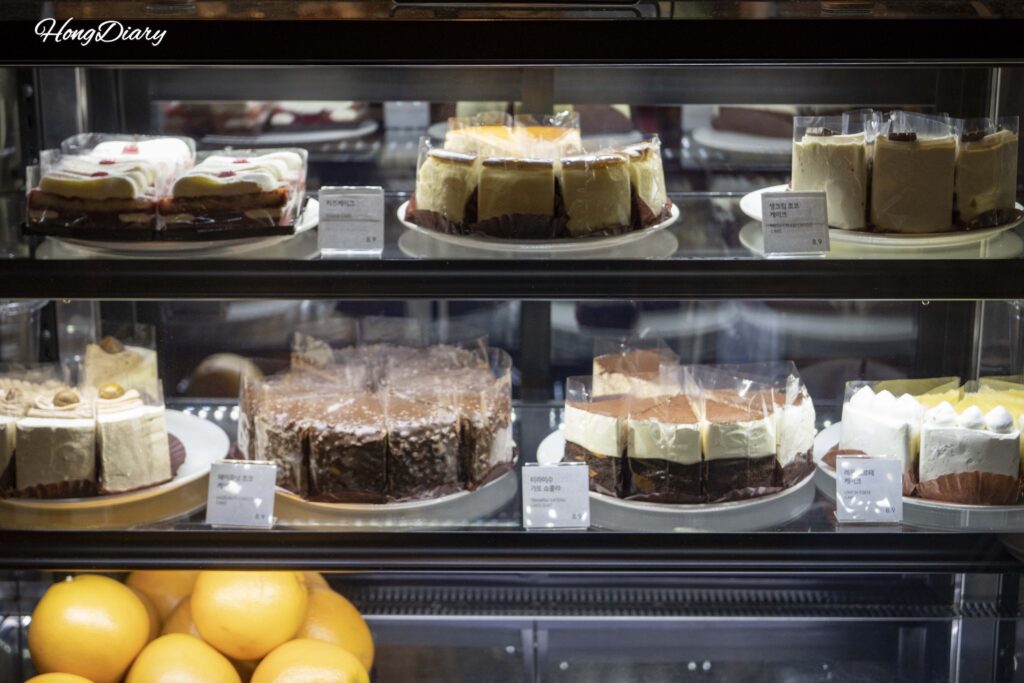 Cake display case at Brown Hands Baekje cafe with tiramisu, cheesecake, and hazelnut chocolate cake slices priced at 8900 won
