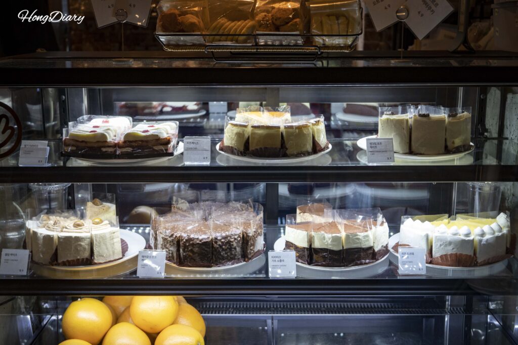 Vitrina de pasteles en Brown Hands Baekje con tiramisú, cheesecake y pastel de chocolate con avellana a ₩8.900 por porción