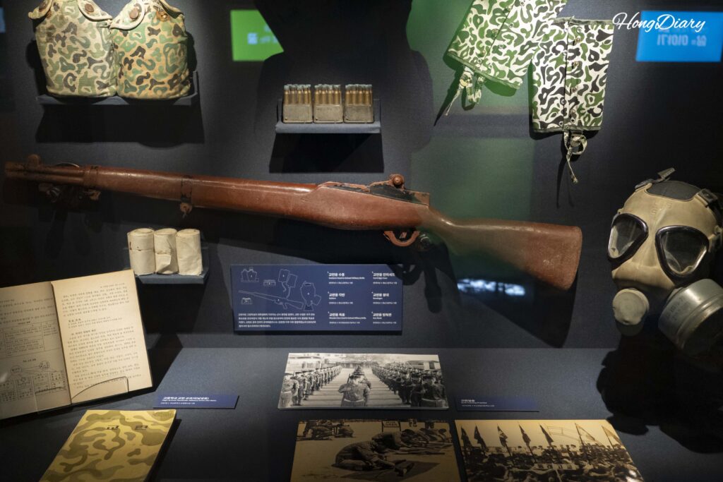 Exposición sobre la instrucción militar escolar en Corea del Sur con fusiles de entrenamiento, máscaras antigás y fotografías, Museo de Historia de la Educación de Busan
