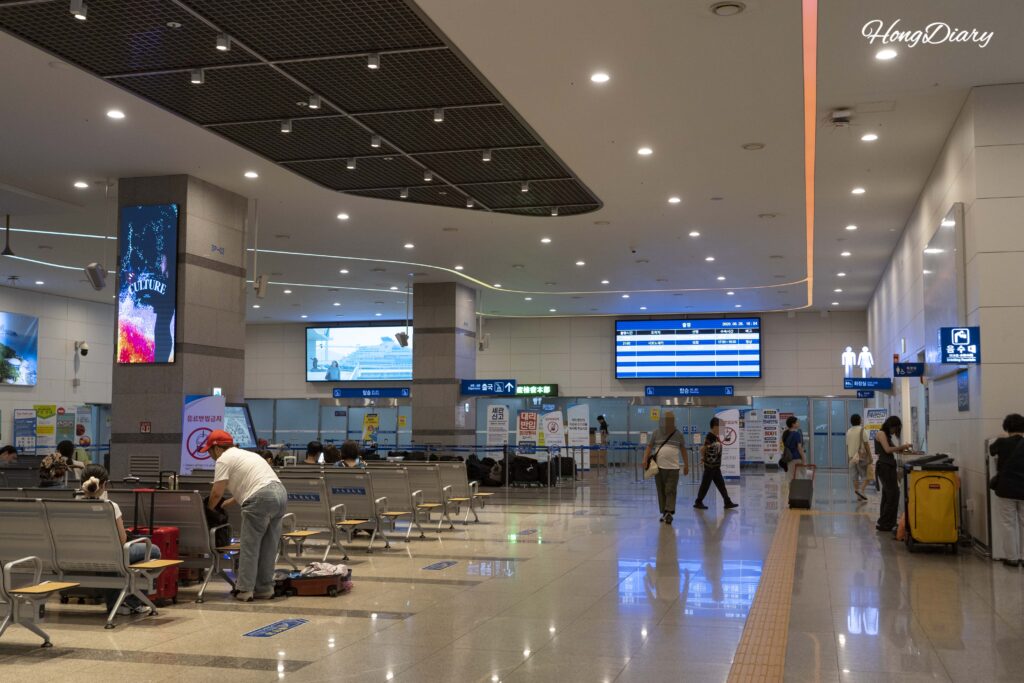 Zona de salidas del tercer piso de la terminal de ferris de Busan con viajeros cerca de los mostradores de taquillas