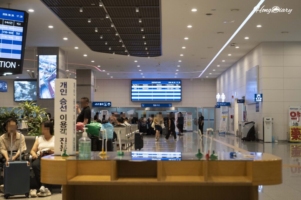 釜山港国際旅客ターミナル3階の出国フロア全景と多くの旅行者、手前に乗船手続き用書類
