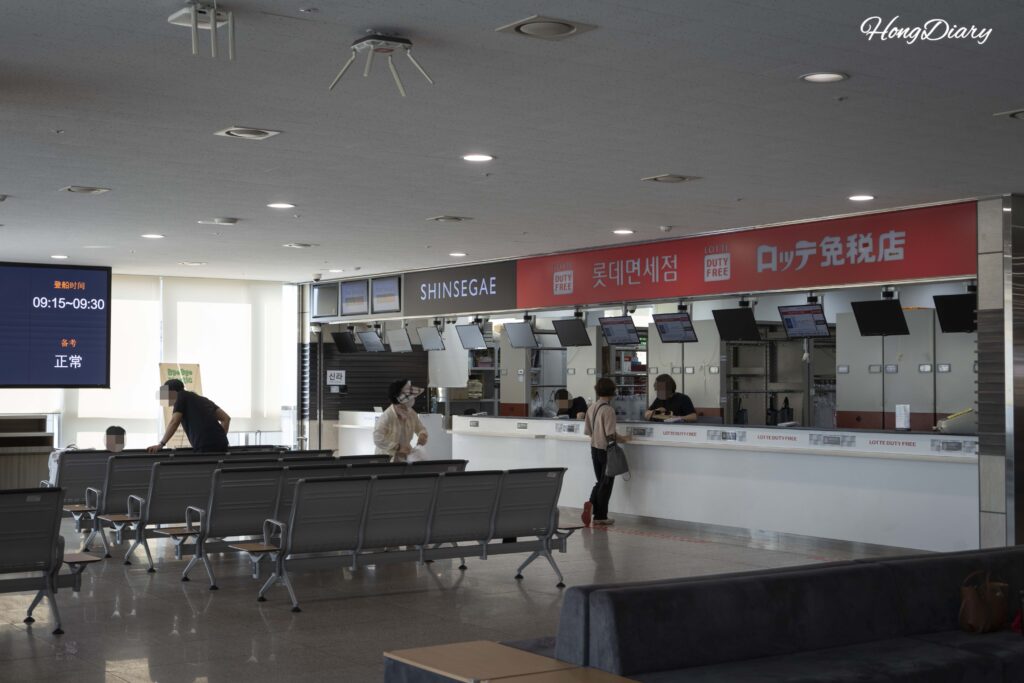 Mostrador de entrega de productos duty-free y pasajeros sentados en la sala de espera de la terminal de ferris de Busan