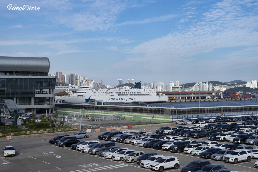 Busan Port International Passenger Terminal exterior with outdoor parking lot and a Fukuoka-bound ferry visible at the berth