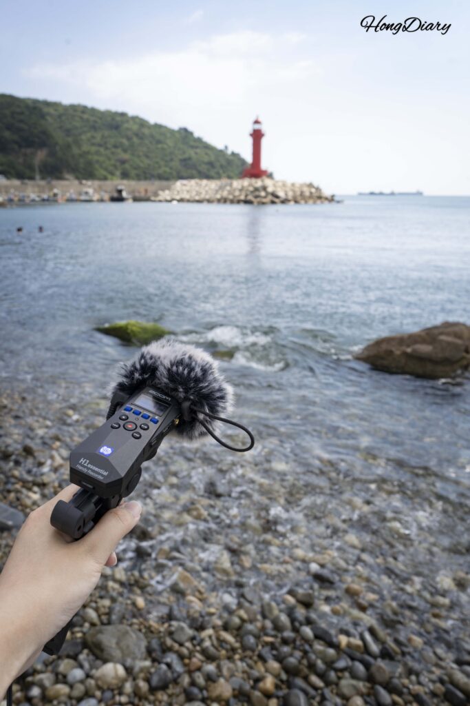 影島・中里海岸でフィールドレコーダーを使って波の音を録音する様子