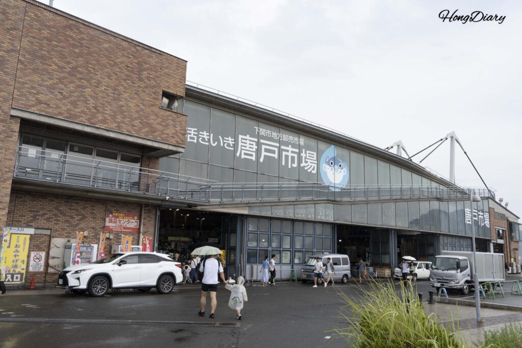 Entrance to Karato Market in Shimonoseki on a rainy day, with visitors holding umbrellas and a child in a rain poncho