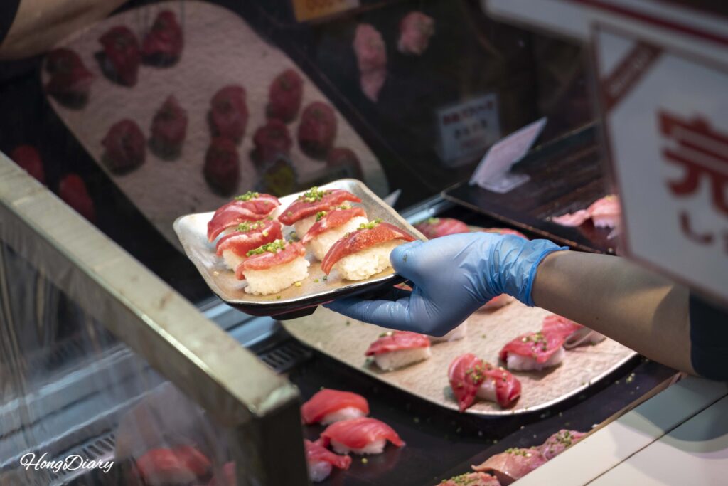A vendor at Karato Market carefully placing sushi pieces into a plastic tray for a customer