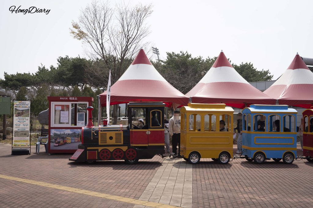 Tren turístico circulando frente al edificio Rookie Zone Derby en Let's Run Park Busan