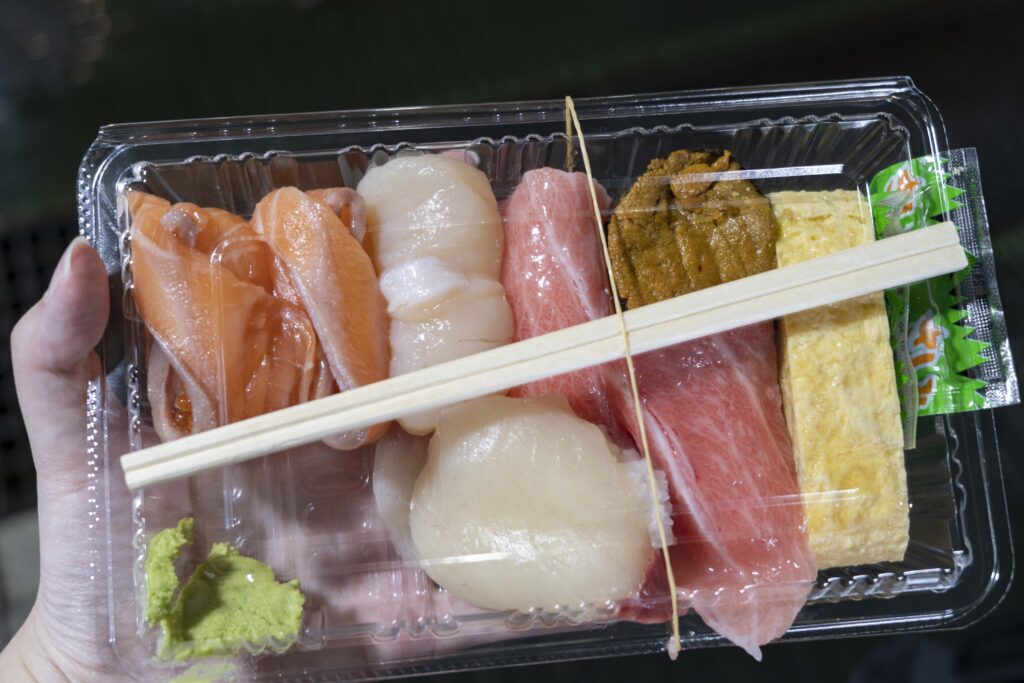 A plastic tray filled with assorted sushi from Karato Market including tuna, scallop, salmon, and sea urchin nigiri