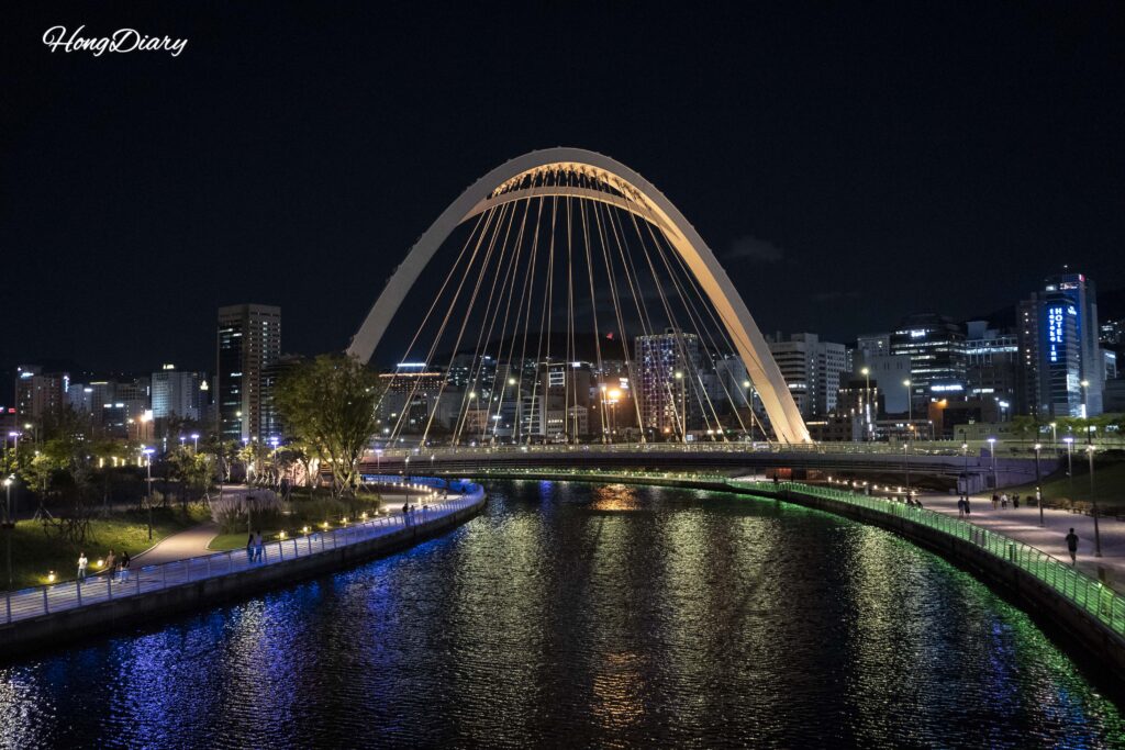 Illuminated pedestrian bridge at North Port Waterfront Park with Busan Station area skyline and high-rise towers at night