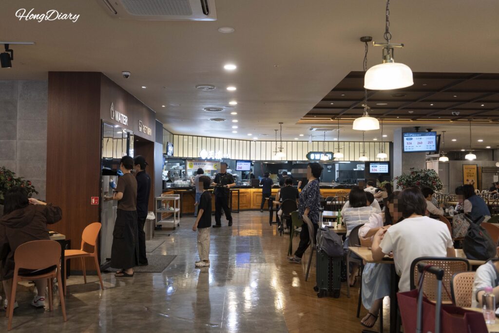Mostrador de recogida de comida, dispensador de agua y zona de devolución de bandejas en Plating, aeropuerto de Gimhae