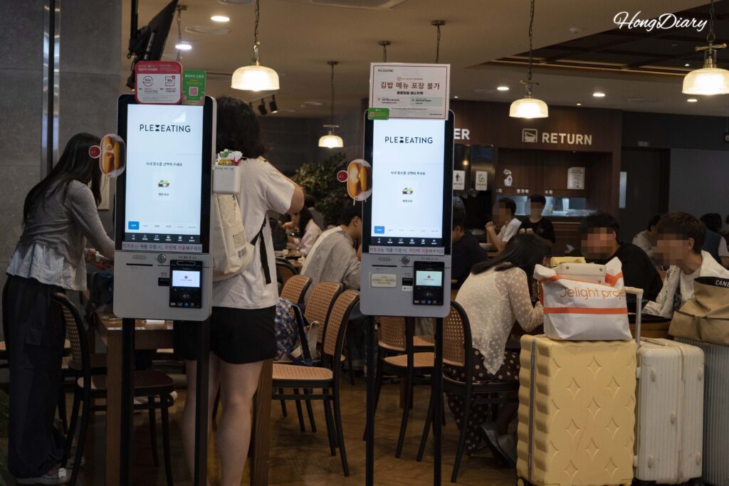 Travelers ordering at touchscreen kiosks inside Plating food court at Gimhae International Airport