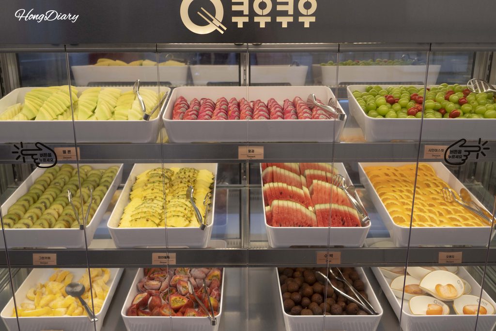 Fresh seasonal fruit display at QooQoo including Shine Muscat grapes, melon, and dragon fruit