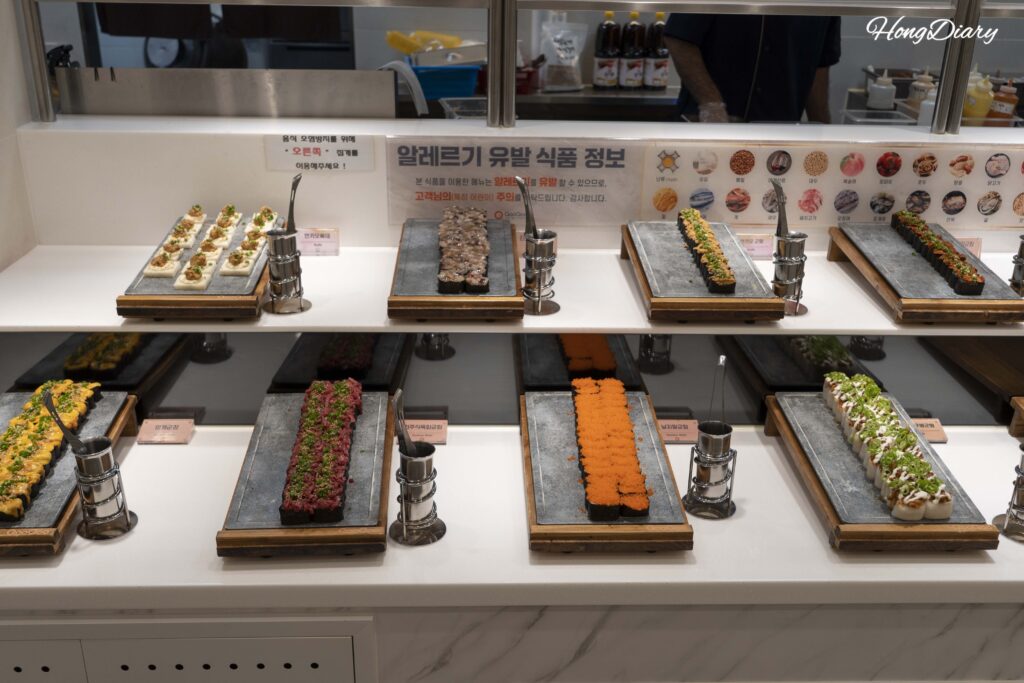 Mostrador de sushi con amplia variedad de nigiri y rollos en el buffet QooQoo