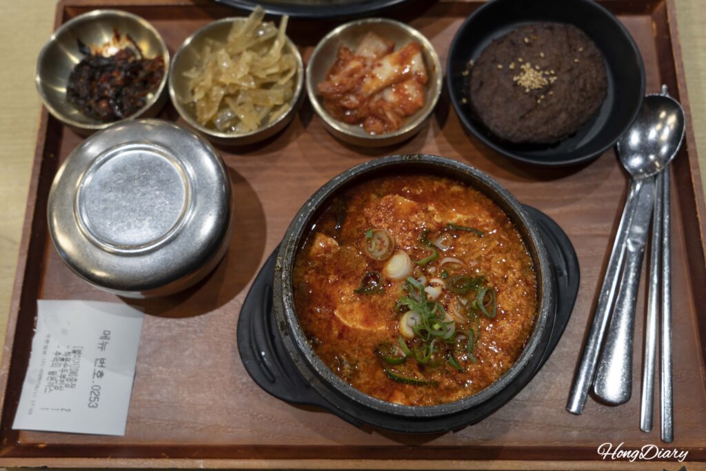 Set completo de sundubu jjigae de mariscos con banchan y tteokgalbi en Plating, aeropuerto de Gimhae