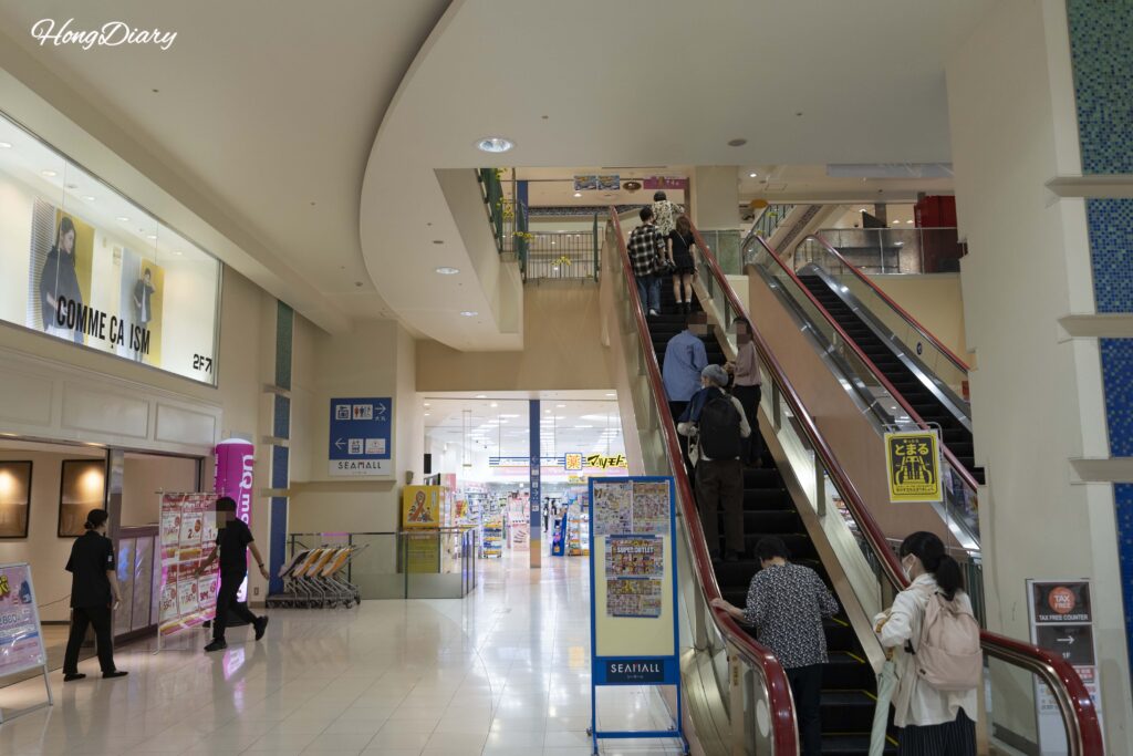 First-floor escalator inside Sea Mall Shimonoseki with shoppers heading to upper levels