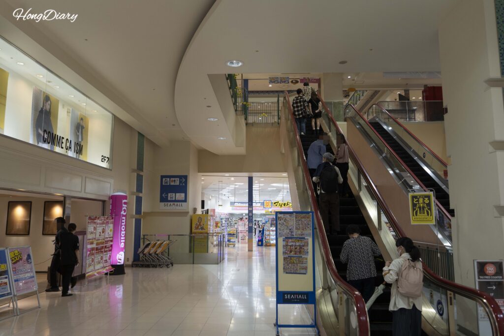 Escaleras mecánicas en la primera planta de Sea Mall Shimonoseki con compradores subiendo a los pisos superiores