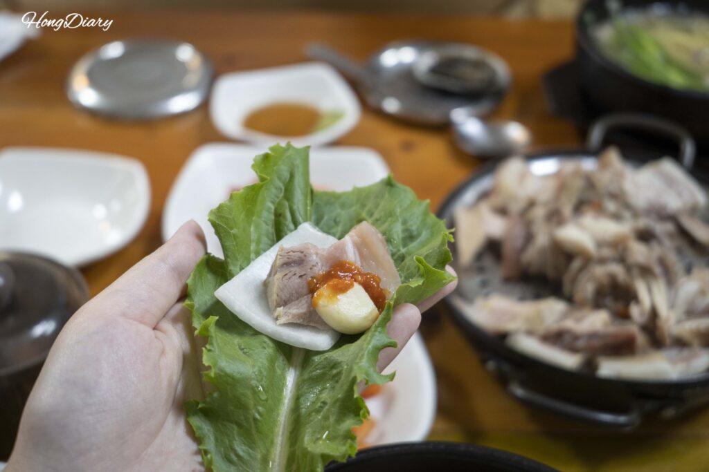 Wrapping boiled pork suyuk with perilla leaf, garlic, and onion in the Korean ssam style at Seonjeongmun Dwaeji Gukbap in Busan