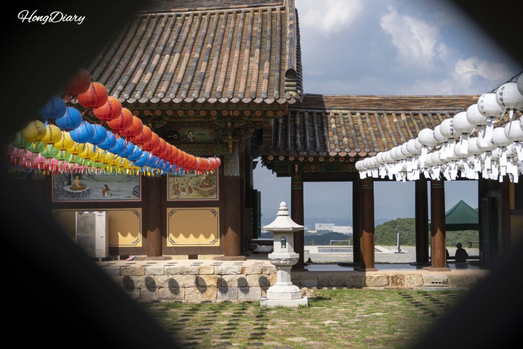 View through gaps in the ceramic Tripitaka stacks showing Seounam Hermitage temple structures and hanging lanterns
