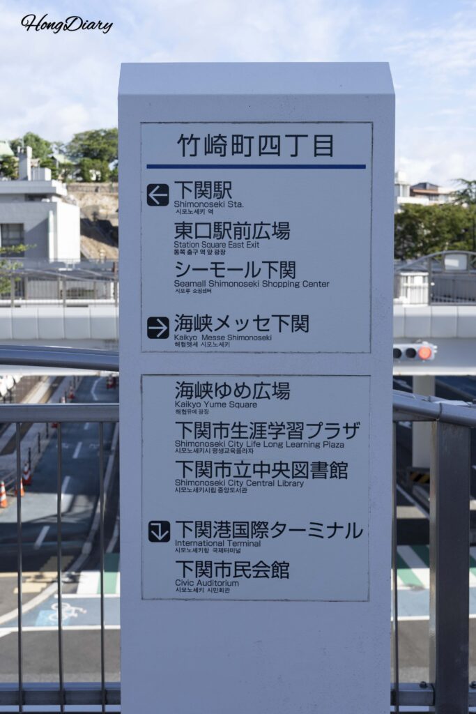 Multilingual signpost outside Shimonoseki ferry terminal showing directions to JR Station, plaza, and shopping center