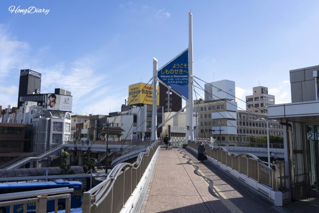 Estructura decorativa de bienvenida a Shimonoseki y paisaje urbano vistos desde la pasarela elevada