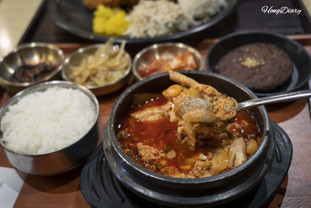 Spooning up soft tofu from a bubbling seafood sundubu jjigae at Plating food court in Gimhae Airport