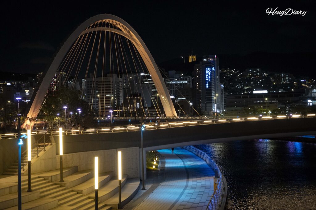 Vista nocturna desde el Puente Peatonal 3 de North Port Waterfront Park mostrando senderos iluminados y el puerto