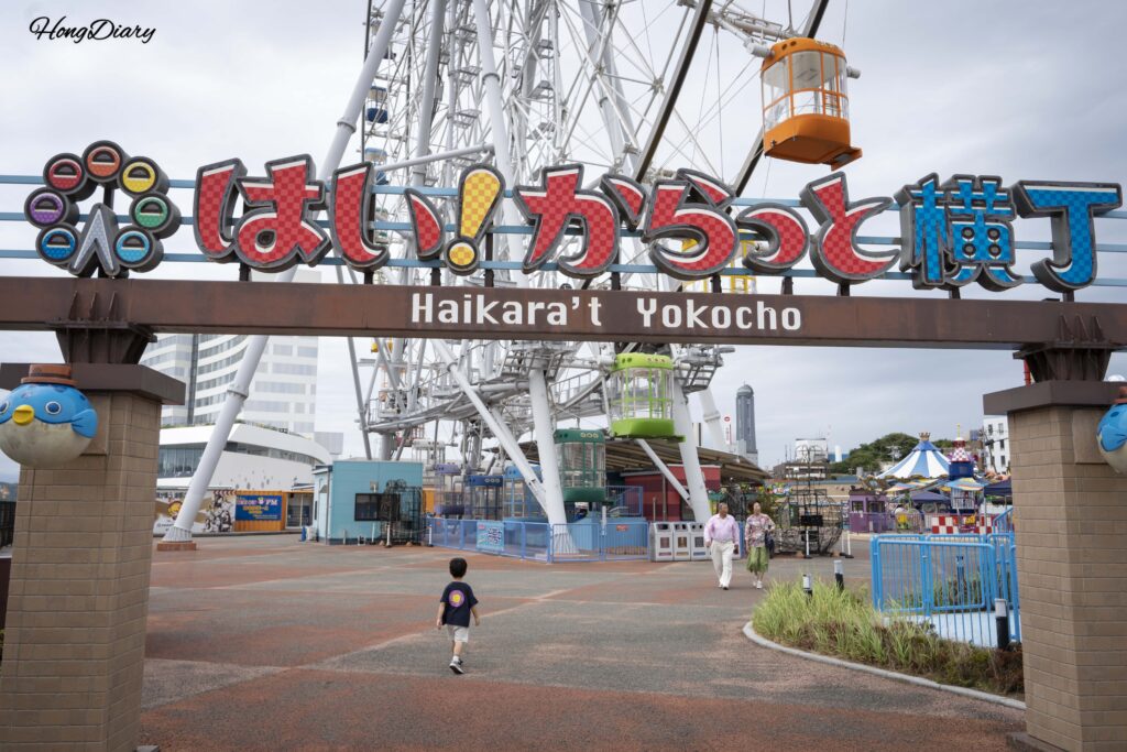 Entrance gate of Haikara't Yokocho amusement park in Shimonoseki with pufferfish statues and a child running toward the rides