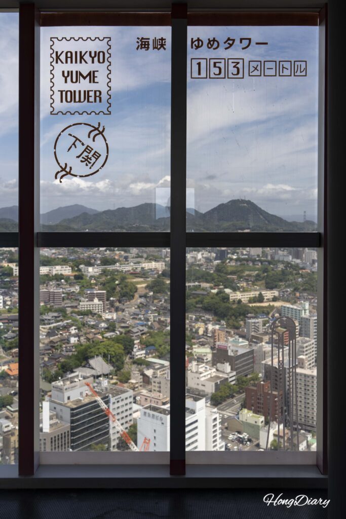 View from the 28th floor of Kaikyo Yume Tower through semi-translucent glass printed with the tower name and postal code creating a postcard-like effect