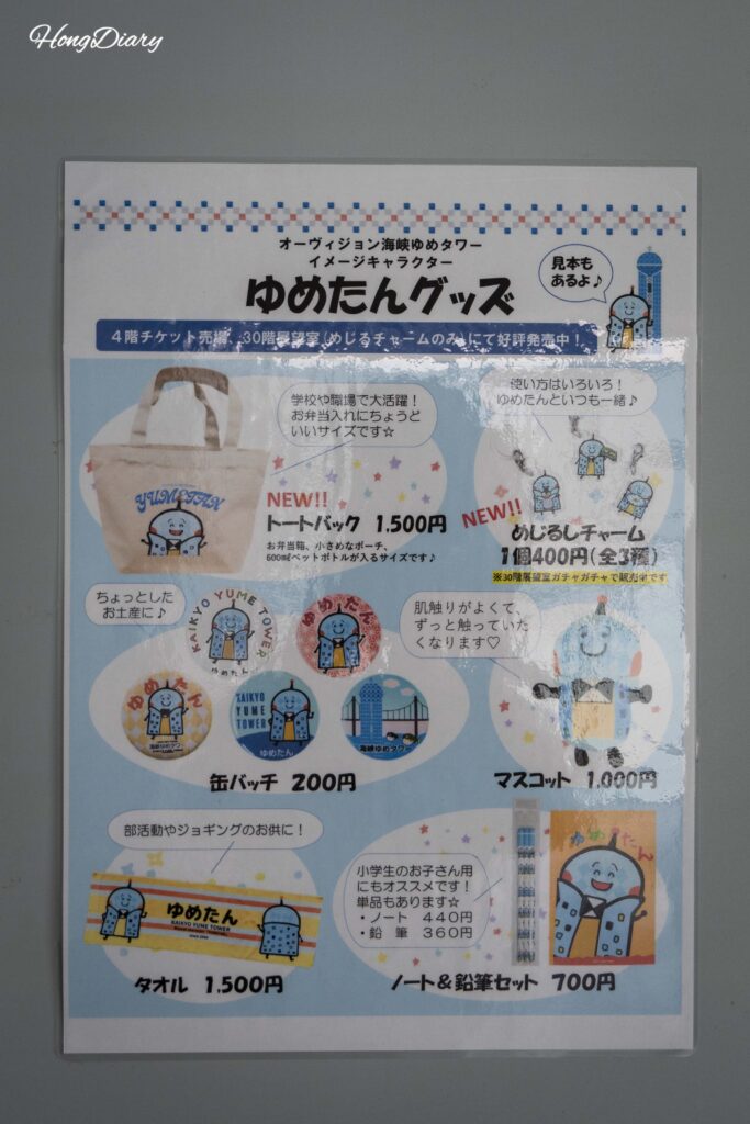 Wall panel on the 30th floor of Kaikyo Yume Tower listing Yume-tan merchandise with prices including eco bags for 1500 yen and keychains for 400 yen