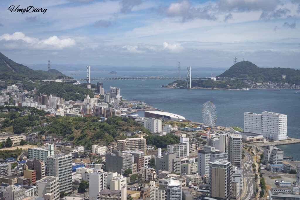 Vista panorámica hacia el este desde el piso 30 de Kaikyo Yume Tower mostrando el Puente Kanmon, el Mercado Karato, el Acuario Kaikyokan y el Estrecho de Kanmon con Mojiko Retro visible en el lado de Kyushu
