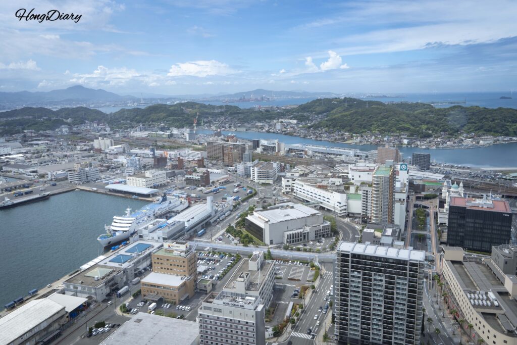 West-facing view from Kaikyo Yume Tower showing the Kampu Ferry docked at Shimonoseki Port International Terminal, Shimonoseki Station, rail tracks, and afternoon sunlight on the sea