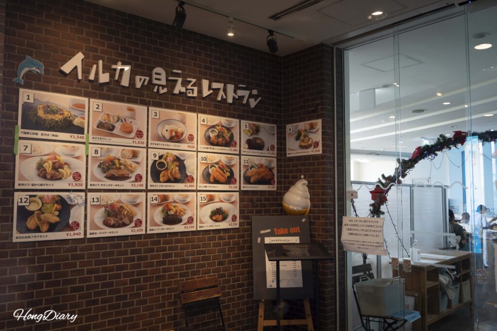 Entrada del restaurante del Acuario Kaikyokan mostrando el tablón de menú con precios de platos incluyendo tempura de fugu y curry infantil
