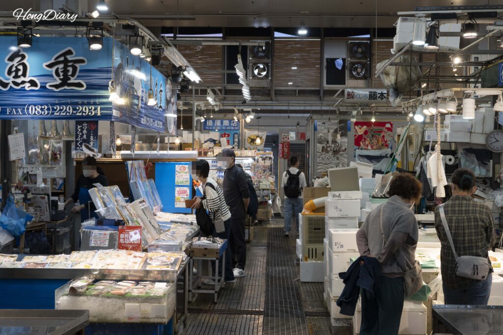 Puestos de mariscos y productos procesados en la zona interior del Mercado Karato con clientes comprando