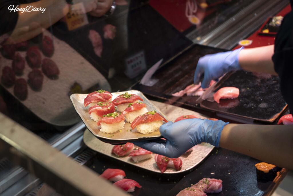 Un vendedor en el Mercado Karato colocando piezas de sushi en una bandeja de plástico para un cliente
