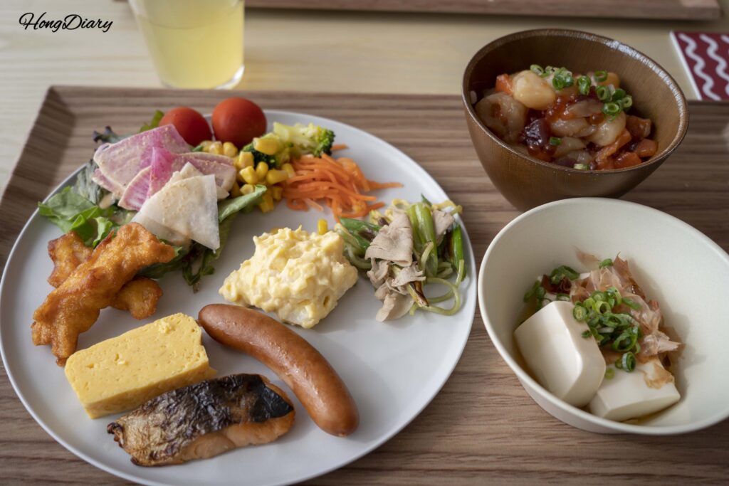 Plato de desayuno con ensalada, salchichas, pescado a la parrilla, tamagoyaki, kaisen don y tofu con salsa de soya en PUKU PUKU